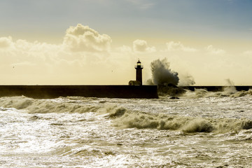 Landscape seascape lighthouse battered by huge waves on Atlantic Ocean with blue green skies and...