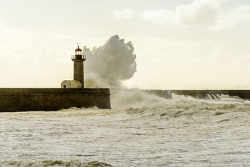 Landscape seascape lighthouse battered by huge waves on Atlantic Ocean with blue green skies and...