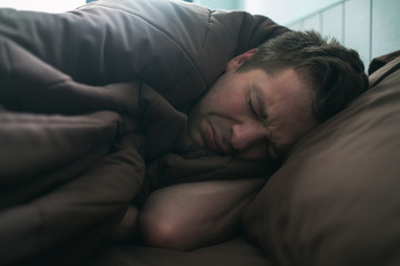 offended caucasian man lie on bed and cover himself with blanket. He is about to cry.