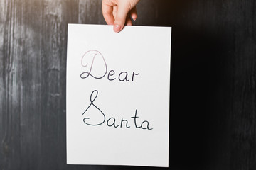 Female hand holding a white sheet of paper with text "Dear Santa"