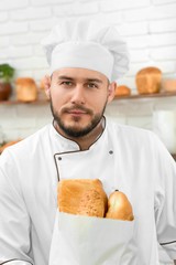 Vertical portrait of a handsome young male baker in his uniform posing proudly at his bakery looking to the camera with confidence profession occupation job employee small business owner.