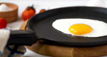 Chicken fried egg in a black frying pan with cherry tomatoes, arugula, salt. Breakfast on a white wooden table. Just cooked food