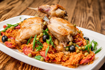 Plate with roasted rabbit leg and vegetable garnish.