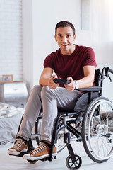 Time for play. Attentive man keeping smile on his face and sitting on the wheelchair while looking...