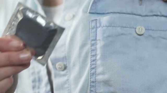 Girl hands holding sealed condom, putting it into pocket of shirt, contraception