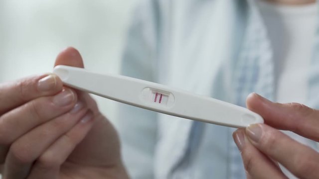 Female hands holding pregnancy test, turning to show two lines, family planning