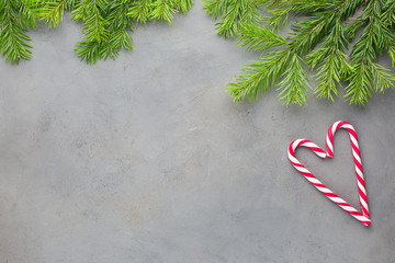 Christmas heart of two red-white candy canes on the gray concrete background with Christmas tree. Beautiful Christmas background. Flat lay, top view