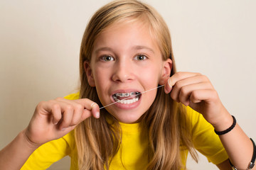 Funny girl with dental braces flossing her teeth. Close-up portrait of pre teen girl with dental...