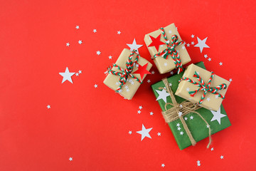 The Christmas gifts packed into a beige and green kraft paper, strewed with red, white paper stars on red background. Top View Flat Lay