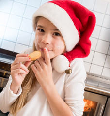 In der Weihnachtsbäckerei nascht junges Mädchen mit Nikolausmütze heimlich an Plätzchen
