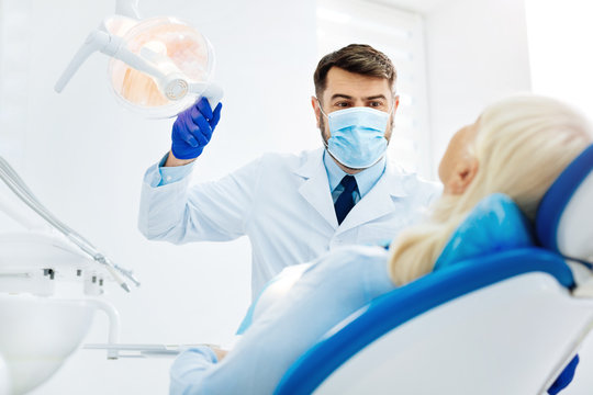 Do not worry. Optimistic dentist with a face mask standing near the patient while touching medical tool
