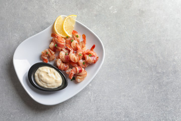 Plate with bacon-wrapped shrimps and tasty sauce on table