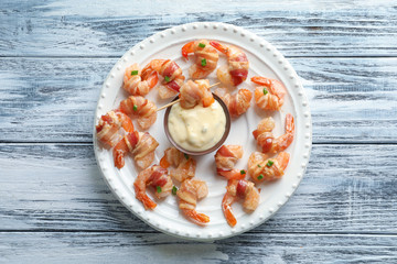Plate with bacon-wrapped shrimps and tasty sauce on wooden table