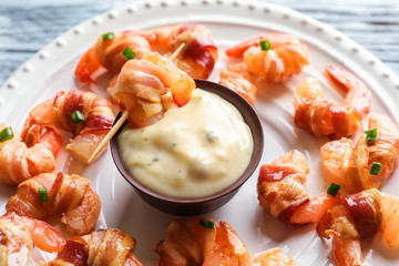 Plate with bacon-wrapped shrimps and tasty sauce, closeup