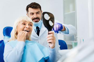 Brilliant job. Close up of positive patient expressing satisfaction while looking in the dental...