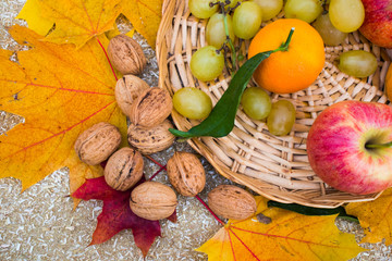 Fruits are in the basket. grapes; apples; clementines; nuts; banana; yellow leaves;