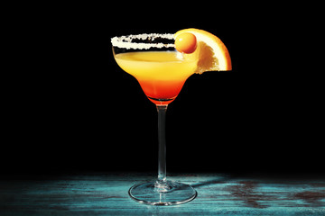 Glass with tasty exotic cocktail on table against black background