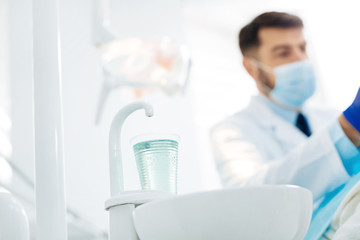 Dental instruments. Close up of a cup of water in the hospital with stomatologist in the background