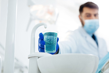 Process of teeth cure. Close up of a plastic cup with water being kept in hand of professional...