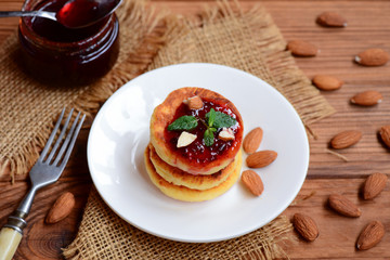 Little syrniki. Fried curd pancakes with berry jam and almonds on a white plate. Russian pancakes recipe. Healthy breakfast idea