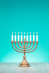 Bronze Hanukkah menorah with burning candles on wooden table front old vintage aquamarine wall background. Holiday greeting card concept. Retro style filtered photo