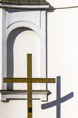 Wooden cross and church wall, Christian religious theme. Reflection of cross on wall of Catholic church on sunny day.