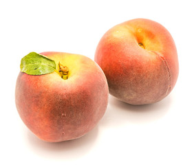 Two whole peaches, one with green leaf, isolated on white background.