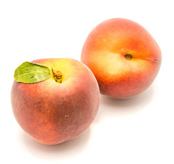 Two whole peaches, one with green leaf, isolated on white background.