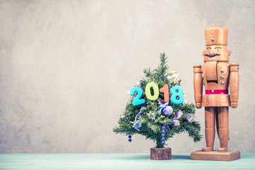 New Year tree with 2018 date and retro old wooden nutcracker toy front textured concrete wall background. Holiday greeting card concept. Vintage instagram style filtered photo