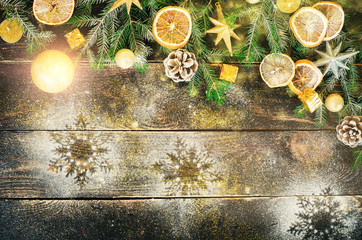 Christmas greeting card with gifts, candle, cones, cinnamon sticks, dry orange, green tree over old dark wood background. Top view with copy space for you text. Snow and bokeh