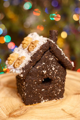 House made of crushed dried prunes, nuts, dates is standing on round wooden board on background of colorful bokeh.