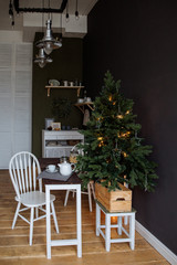 The dining room is decorated by Christmas. Wooden furniture. On a table ware for a breakfast. Nearby the Christmas fir-tree with garlands.