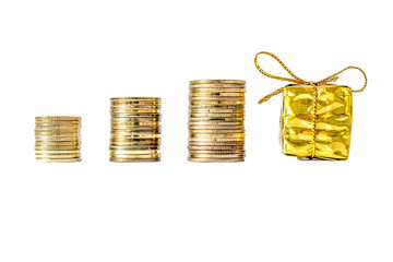 Gift box in gold packing bandaged with a bow next to coins column close-up isolated on white background