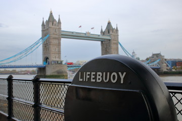 Koło ratunkowe w czarnym pokrowcu na brzegu Tamizy, w tle niewyraźny most Tower Bridge i rzeka, Londyn, Wielka Brytania - obrazy, fototapety, plakaty