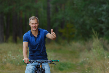 Man shows thumb up, riding on bicycle in forest