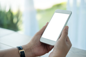 Mockup image of hands holding white mobile phone with blank screen on table in cafe