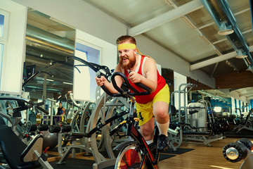 Fototapeta na wymiar A fat man is training on an exercise bike in the gym.
