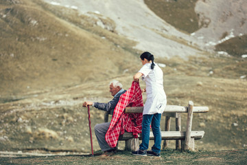 Nurse helping elderly senior man to walk on frash air outdoor.