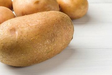 Uncooked, fresh crop of potatoes on wooden table of white planks background, close-up view