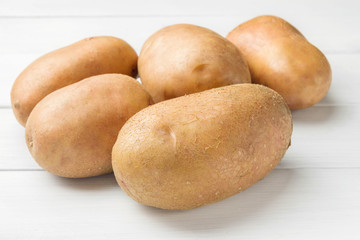 Uncooked, fresh crop of potatoes on wooden table of white planks background, close-up view