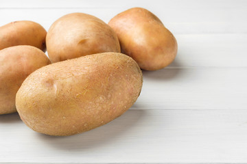 Uncooked, fresh crop of potatoes on wooden table of white planks background, close-up view