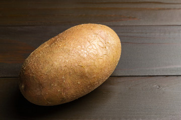 Uncooked, fresh whole one potato on wooden table of dark brown planks background, close-up view
