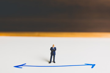 Miniature Businessman standing on arrow pathway , Business decision concept.