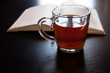A glass mug with tea and a lemon slice, notebook with blank pages, black pen on dark desk