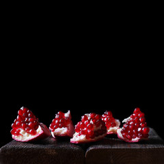 A pomegranate on a wooden table with a dark background. Garnet seeds in beautiful soft light in a...