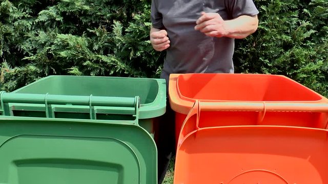 A man putting cardboard and green waste into separate, large plastic recycle bins.