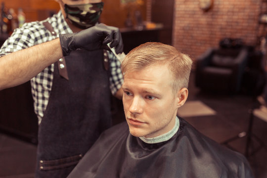 Handsome hairdresser cutting hair of male client. Men hairstylist serving client at vintage barber shop.