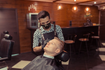 Handsome blonde man having his hair cut by hairdresser at the retro barbershop