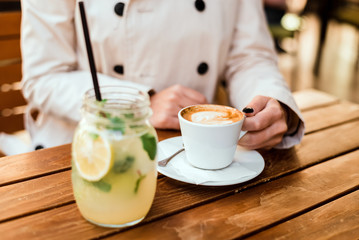 Close up of woman holding cup of coffee on wooden table.