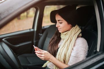 Beautiful woman smiling while sitting in the car. Girl is using a smartphone